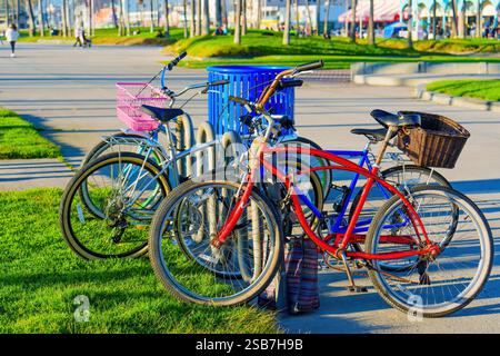 Los Angeles, Kalifornien - 18. Dezember 2024: Sammlung farbenfroher Fahrräder, die in der Nähe eines blauen Abfalleimers auf dem Weg am Venice Beach geparkt sind und beac zeigen Stockfoto