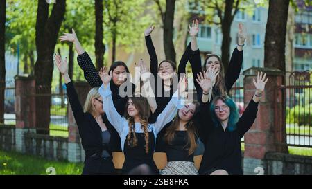 Gruppe fröhlicher Schülerinnen, die nach der Schule ihre Hände heben, um ihre Freizeit zu genießen Stockfoto