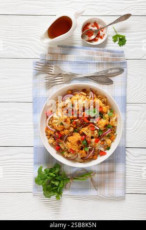 Gebratener Blumenkohl-Quinoa-Salat mit Walnüssen, rotem Pfeffer, Zwiebeln und Koriander in weißer Schüssel auf weißem Holztisch, vertikale Ansicht Stockfoto