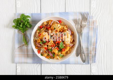 Gebratener Blumenkohl-Quinoa-Salat mit Walnüssen, rotem Pfeffer, Zwiebeln und Koriander in weißer Schüssel auf weißem Holztisch mit Gabeln, Blick von oben Stockfoto