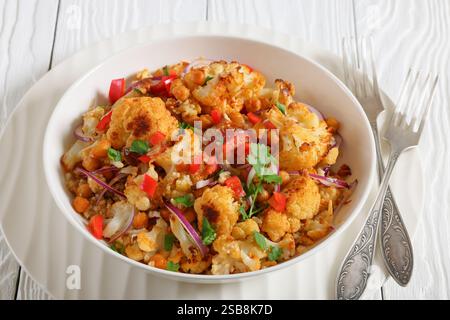 Gebratener Blumenkohl-Kichererbsen-Quinoa-Salat mit Walnüssen, rotem Pfeffer, Zwiebeln und Koriander in einer weißen Schüssel, Nahaufnahme Stockfoto