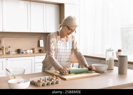 Inspirierte Hausfrau mittleren Alters im Schürzenrollenteig in der Küche Stockfoto