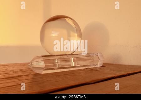 Kugelkugel aus klarem Kristall, die auf einem Punkt aus klarem Quarzkristall auf einer Holzoberfläche aufliegt Stockfoto