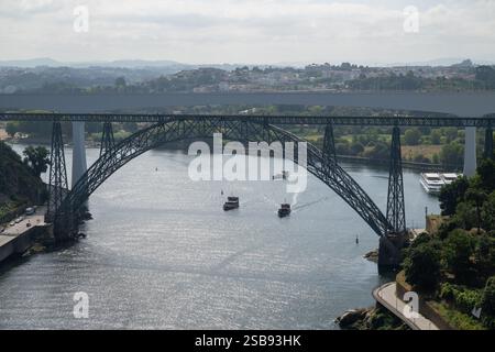 Die Brücke Dona Maria Pia und die Brücke Sao Joao überspannt den Fluss Douro mit malerischen Hügeln und Booten auf ruhigem Wasser Stockfoto