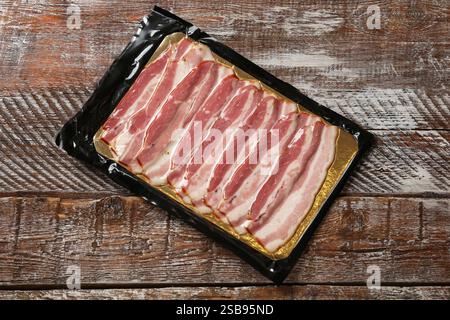 Packung mit geschnittenem Speck auf Holztisch, Blick von oben Stockfoto