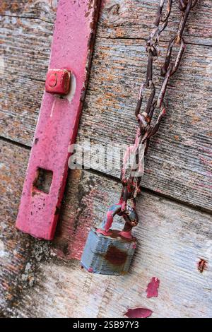 Eine rostige Kette hängt an einem rostigen Schloss. Das Schloss ist rot und die Kette ist silber Stockfoto