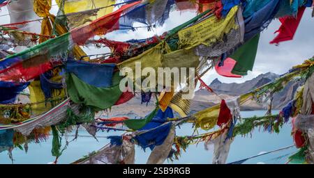 Zerrissene alte Gebetsfahnen flattern im Wind und Schnee über dem Tilicho-See. Stockfoto