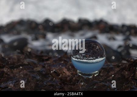 Der Lensball liegt auf einem Bett aus getrocknetem Gras und Kieselsteinen. Die Kristallkugel reflektiert die Umgebung, einschließlich des Himmels und der Steine in der Nähe Stockfoto