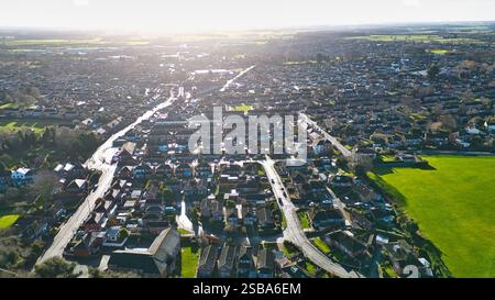 Aus der Vogelperspektive eines Wohngebiets mit zahlreichen Häusern, Straßen und einem großen grünen Feld. Die Sonne scheint hell und wirft Schatten Stockfoto