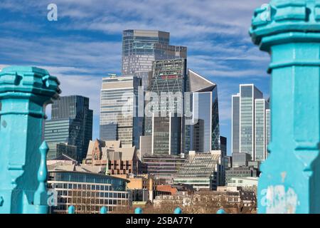 Moderne Wolkenkratzer und ältere Gebäude in London, betrachtet durch blaublaues Brückengeländer unter einem teilweise bewölkten blauen Himmel. Das Bild zeigt eine Mischung aus AR Stockfoto