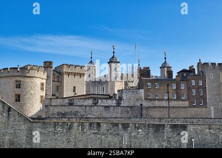 Außenansicht des Tower of London mit verschiedenen Steinstrukturen, einschließlich Türmen, Mauern und Gebäuden, unter einem klaren blauen Himmel Stockfoto