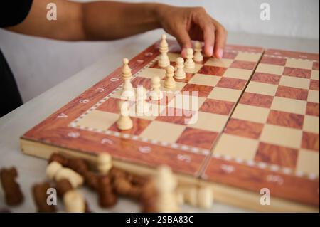 Man sieht, wie eine Person Schachfiguren auf einem traditionellen hölzernen Schachbrett aufbaut und sich auf ein strategisches Spiel in einer fokussierten Umgebung vorbereitet. Stockfoto