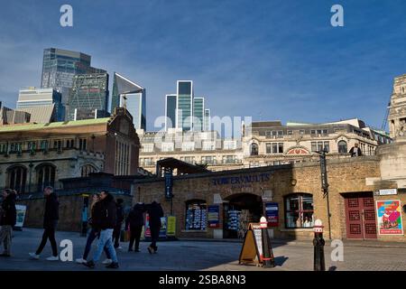 Moderne Wolkenkratzer erheben sich über älteren Ziegelgebäuden und einem Souvenirshop in London unter einem klaren blauen Himmel. Die Leute laufen auf der Straße. Stockfoto