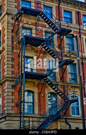 Außenansicht eines Ziegelgebäudes mit mehreren miteinander verbundenen Metalltreppen, die sich über mehrere Stockwerke erstrecken. Das Gebäude verfügt über 1 Stockfoto