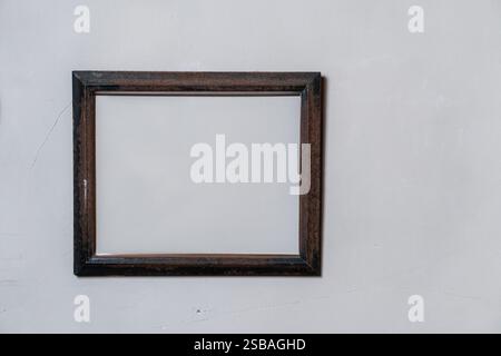Ein leerer Bilderrahmen aus Holz, der an einer einfachen Wand hängt. Der Rahmen hat eine dunkle Oberfläche und ein schlichtes Design, was einen klassischen Look schafft. Stockfoto