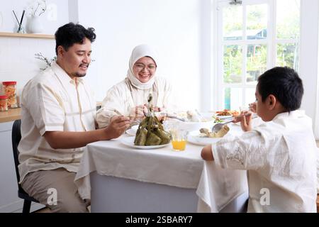 Junge asiatische muslimische Familie, Vater, Mutter und zwei Kinder essen Ketupat Lebaran zusammen, feiern Idul Fitri Eid Al Fitr Stockfoto