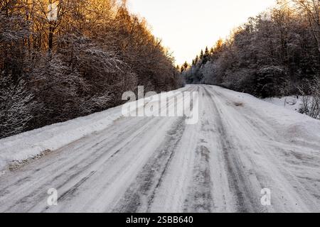 Oberfläche der rutschigen Eisstraße im Wald bei Wintersonnenuntergang Stockfoto