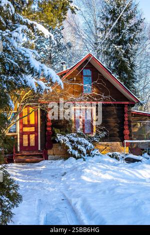 Schneebedeckter Pfad und farbenfrohes Blockhaus im Dorf am sonnigen Wintertag Stockfoto