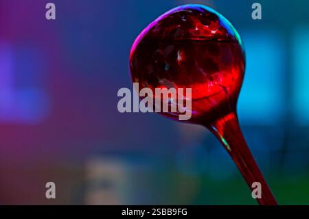Ein auffälliges Makrofoto nimmt einen einzelnen roten Wassertropfen auf, der auf einem unscharfen blauen Hintergrund aufgehängt wird und ein faszinierendes Farbenspiel erzeugt Stockfoto