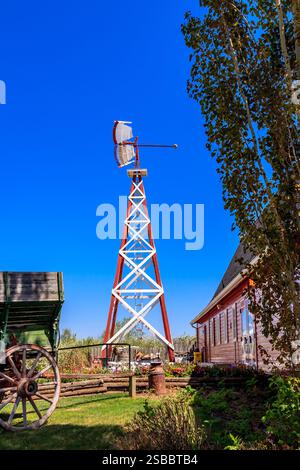 Eine Windmühle steht vor einem Haus. Die Windmühle ist hoch und hat eine rote und weiße Farbe. Der Himmel ist blau und klar Stockfoto
