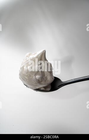 Eiweiß oder mit Zucker geschlagene Baisons auf einem schwarzen Löffel auf weißem Hintergrund. Nahaufnahme. Leerzeichen für Text. Hochwertige Fotos Stockfoto