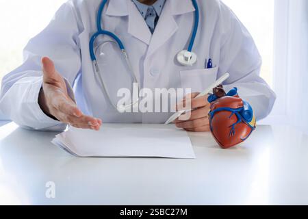 Ein Arzt in einem weißen Mantel mit einem Stethoskop um den Hals spricht mit einem Patienten über Herzgesundheit. Stockfoto