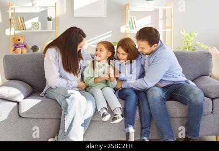 Glückliche Familie, die sich auf dem Sofa im Wohnzimmer entspannt, während die Eltern lachen und die Kinder kitzeln. Stockfoto