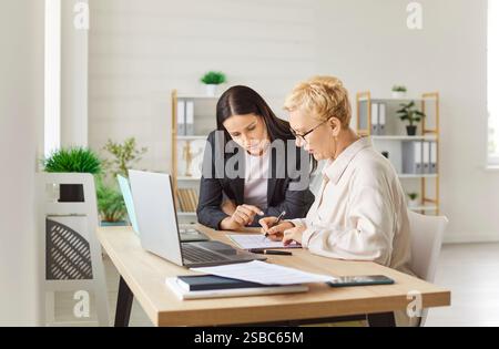Zwei fokussierte weibliche Kollegen sitzen in modernen Büros, überprüfen die Daten auf einem Blatt und arbeiten als Team. Stockfoto