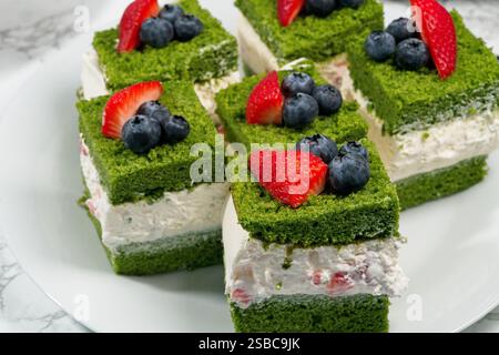 Eine Schicht grüner Biskuitkuchen wird mit Schlagsahne, Heidelbeeren und Erdbeeren belegt. Stockfoto