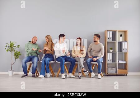 Junge Menschen in lässiger Kleidung sitzen auf Stühlen in der Reihe und warten auf die Umkehr der Intervieweinladung Stockfoto