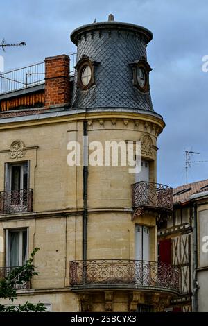 Ein historisches französisches Gebäude mit einem charakteristischen runden Turm, kunstvollen Eisenbalkonen und Schieferdächern unter einem bewölkten Himmel. Stockfoto