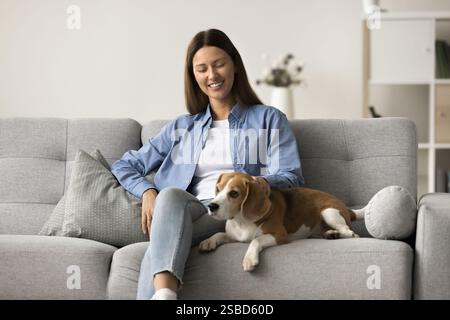 Schöne junge Frau, die auf dem Sofa sitzt, mit einem hübschen Beagle-Hund Stockfoto
