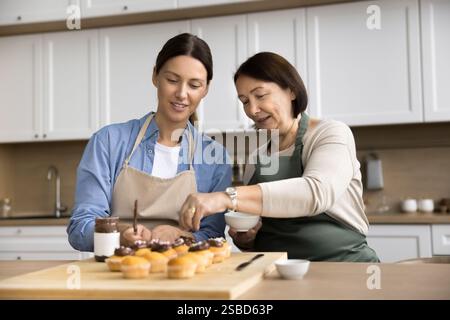 Ältere Frau aus den 60er Jahren, ihre junge Erwachsene Tochter aus den 35er Jahren, die das Dessert zubereitet Stockfoto