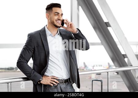 Mobile Kommunikation. Gutaussehender Mann Aus Dem Nahen Osten, Der Auf Dem Handy Am Flughafen Spricht Stockfoto