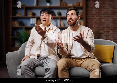 Fans schauen sich ein Spiel an, feiern den Sieg, begeisterte Freunde beim Fernsehen, zwei Freunde haben sich auf einem gemütlichen Sofa unterhalten und lachen Stockfoto