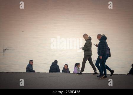 BELGRAD, SERBIEN - 1. DEZEMBER 2024: Ein serbisches Paar schlendert entlang der Donauküste in Zemun und überprüft ihre Smartpjones. Diese legere Szene spiegelt sich wider Stockfoto