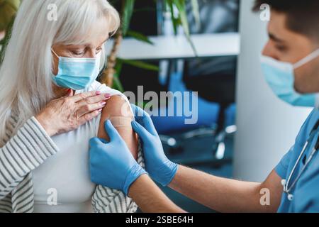 Seniorin wird gegen Grippe geimpft, Arzt wendet Pflaster an Stockfoto