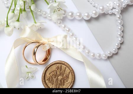 Eheringe gebunden mit Band, Liebesbrief, schöne Blumen und Perlenkette auf hellem Hintergrund, flache Lay Stockfoto