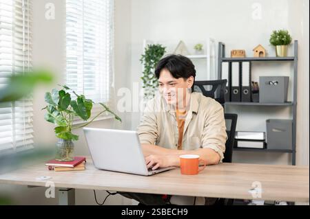 Ein gutaussehender, positiver asiatischer Geschäftsmann arbeitet an seinem Laptop im Büro, liest E-Mails oder surft im Internet. Stockfoto