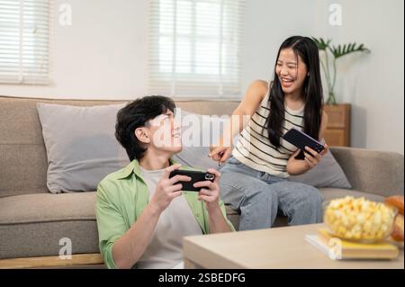Ein überfröhliches, glückliches asiatisches Paar spielt gerne gemeinsam ein Rennspiel auf ihrem Smartphone und hat eine lustige Zeit zu Hause. Spaß, Wettbewerb, Unterhaltung Stockfoto
