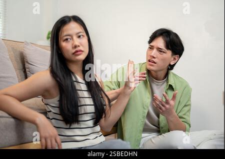 Eine toxische Beziehung bei einem jungen Paar. Ein unglückliches asiatisches Paar sitzt im Wohnzimmer, streitet und hat einen Konflikt, unfähig, jedes Othe zu verstehen Stockfoto