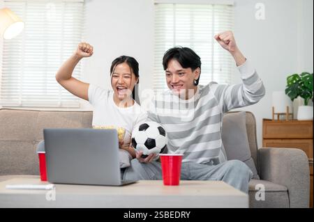 Ein aufgeregtes und glückliches junges asiatisches Paar feiert den Sieg ihrer Fußballmannschaft und unterstützt ihre Lieblingsmannschaft Stockfoto
