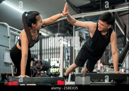 Eine fröhliche asiatische Frau und ein Mann, ein Paar oder Freunde, geben sich beim Auflegen von Liegestützen und beim gemeinsamen Training im Fitnessstudio eine hohe fünf. Er Stockfoto