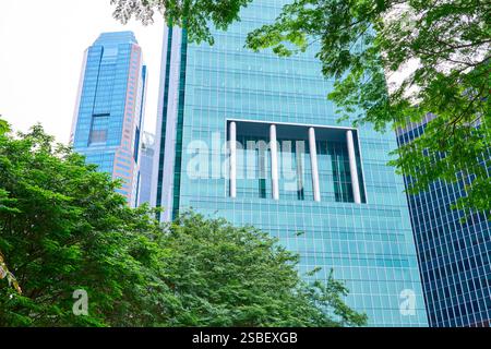 Üppig grüne Bäume umrahmen die eleganten Glasfassaden moderner Wolkenkratzer im zentralen Geschäftsviertel singapurs und bieten eine harmonische Mischung aus Natur Stockfoto