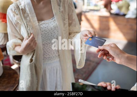 Eine Nahaufnahme einer zufriedenen asiatischen Kundin, die ihre Kreditkarte an eine Ladenkasse übergibt, um ihre Artikel zu bezahlen, während sie in einem Bekleidungsgeschäft einkaufen. Stockfoto
