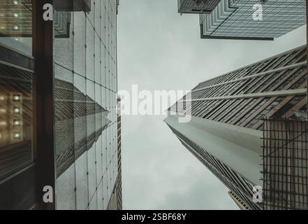 Eine Nahaufnahme aus der Nähe fängt die imposanten Wolkenkratzer von Hongkong ein, deren gewaltige Formen einen gedämpften Himmel durchdringen. Das Bild betont den Buildi Stockfoto