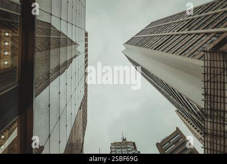 Bei einer Nahaufnahme aus dem niedrigen Winkel werden die Wolkenkratzer in Hongkong sichtbar, deren imposante Strukturen den Rahmen vor einem gedämpften Himmel füllen. Stockfoto