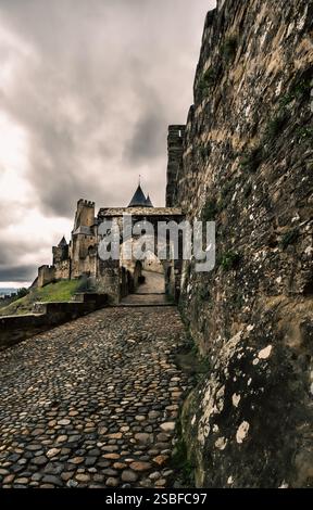 Kopfsteinpflasterweg führt zum historischen Aude-Tor, um an einem bewölkten Tag in die Festung von Carcassonne, Frankreich, zu gelangen. Stockfoto