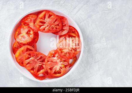 Frische Tomatenscheiben im Kreis auf weißer Platte angeordnet, hellgrauer strukturierter Hintergrund, Draufsicht, Kopierraum Stockfoto