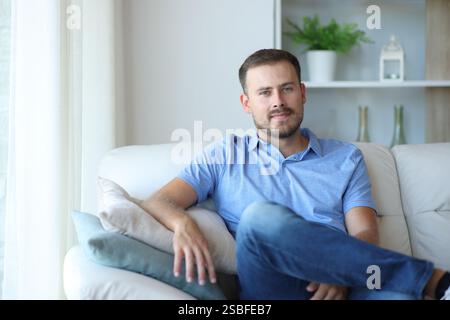 Vorderansicht Porträt eines entspannten Mannes, der zu Hause auf einer Couch sitzt und Sie anschaut Stockfoto
